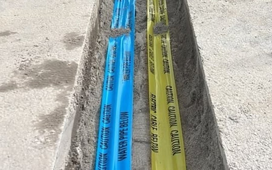 Blue water pipe and yellow electric cable warning tapes laid in a service trench